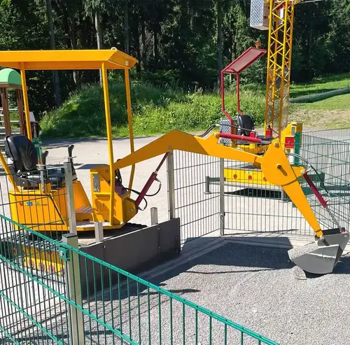 Spielebagger & Kinderkran | Wasserkuppe Ein gelber Spielebagger in parkähnlicher Umgebung.