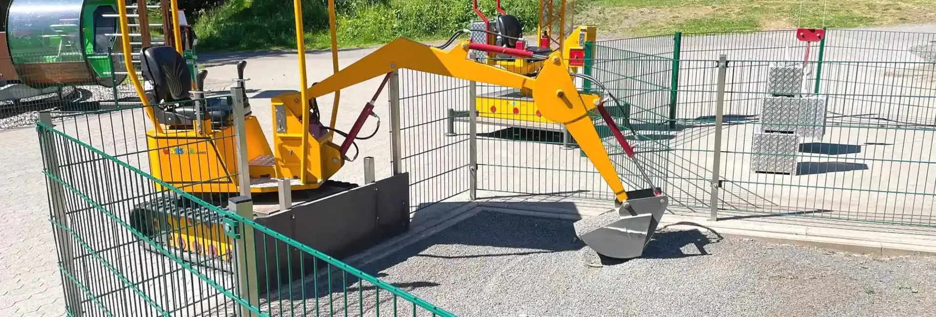 Spielebagger & Kinderkran | Wasserkuppe Ein gelber Spielebagger in parkähnlicher Umgebung.