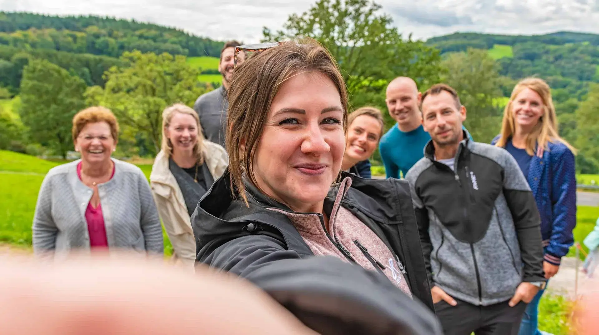 Eine junge Frau macht ein Selfie von sich und ihrer Reisegruppe. Alle sind am lachen und genießen die Natur. Erleben sie schöne Momente und tolle Gruppenangebote am Erlebnisberg in Altenberg.